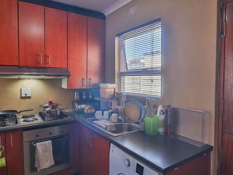 A functional kitchen featuring wood-finish cabinetry, a gas hob with extractor, built-in oven, and a stainless steel sink with a window view.
