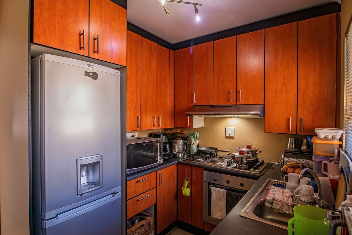 Compact kitchen featuring warm-toned wooden cabinetry, a gas hob with extractor fan, built-in oven, and stainless steel sink with ample counter space.