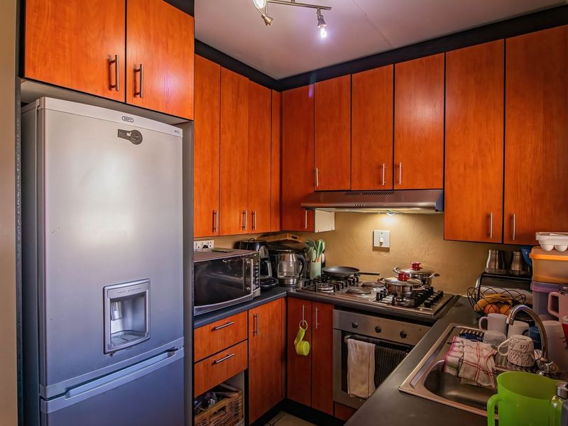 Compact kitchen featuring warm-toned wooden cabinetry, a gas hob with extractor fan, built-in oven, and stainless steel sink with ample counter space.