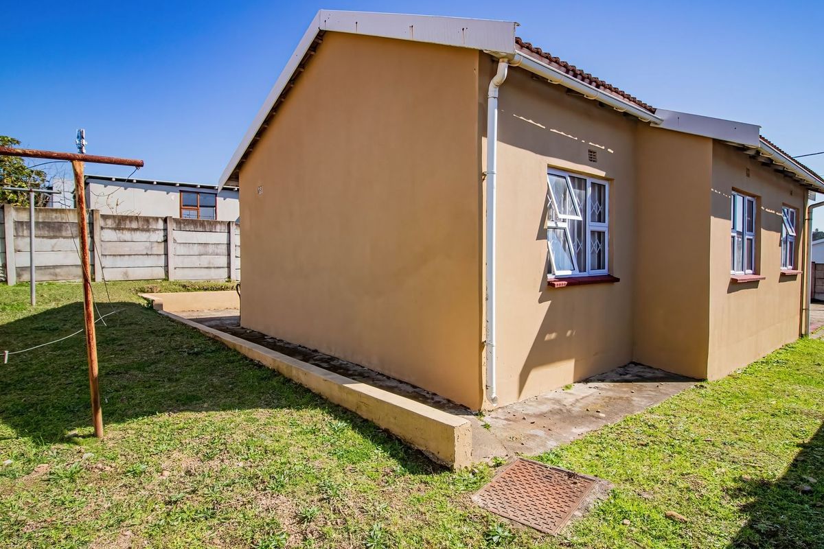 Rear view of the property featuring a tiled roof, aluminium window frames with security bars, and a surrounding lawn area with precast boundary walls.