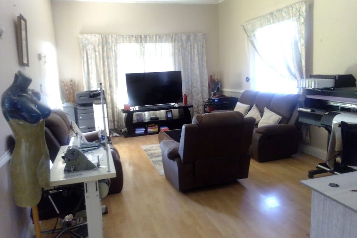 A living room featuring laminate flooring and coving, currently utilized as a multi-purpose living and workspace area.