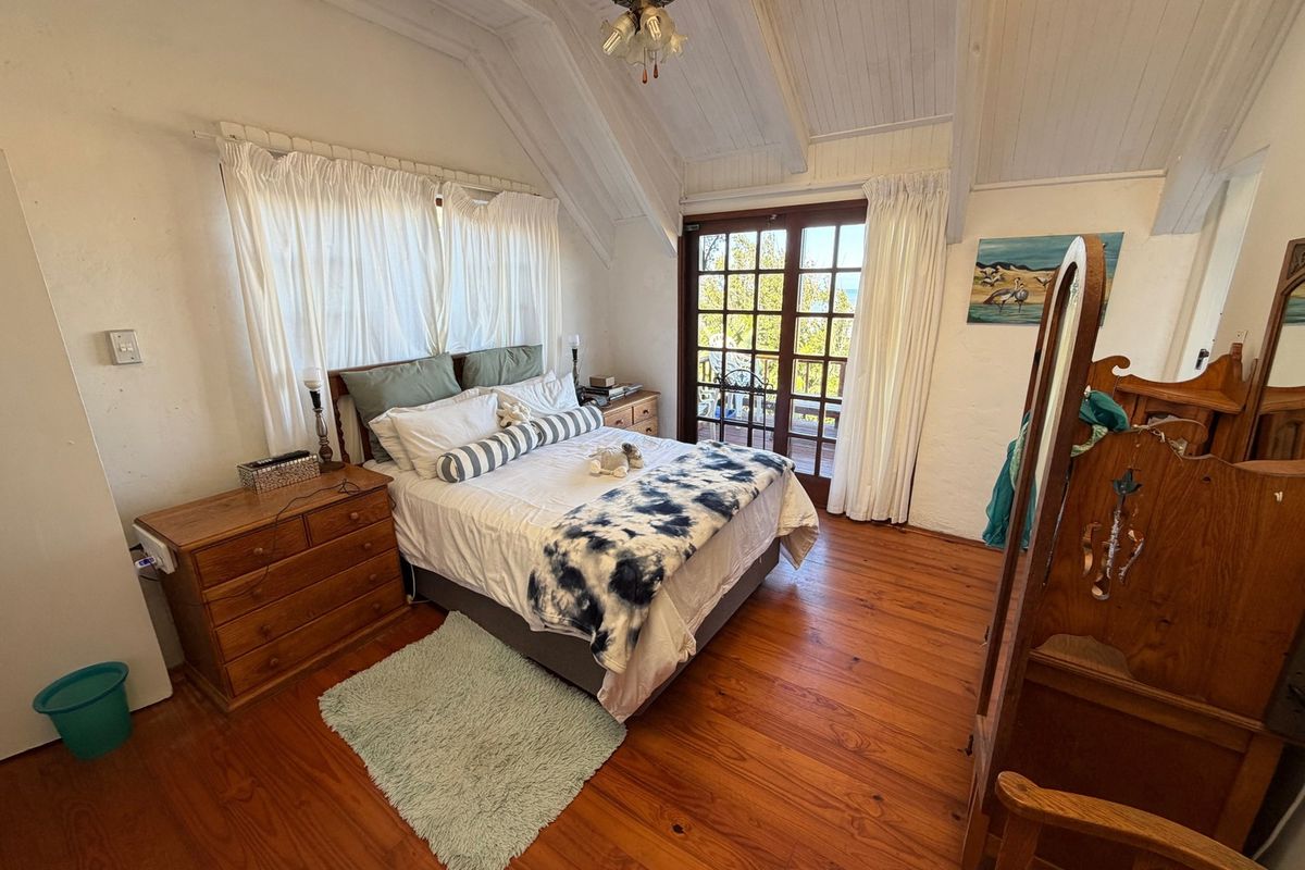 A cozy bedroom featuring vaulted timber ceilings, warm hardwood flooring, and direct access to an outdoor balcony through classic French doors.