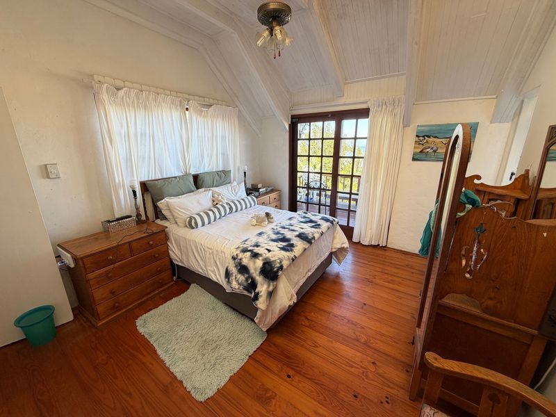 A cozy bedroom featuring vaulted timber ceilings, warm hardwood flooring, and direct access to an outdoor balcony through classic French doors.