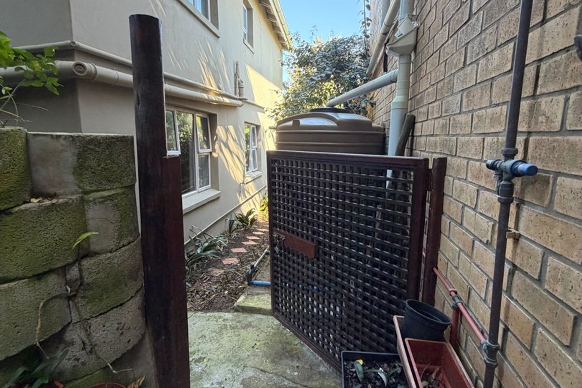A narrow side passage featuring a water tank, brick walling, concrete paving, and a timber gate providing access to the rear of the property.
