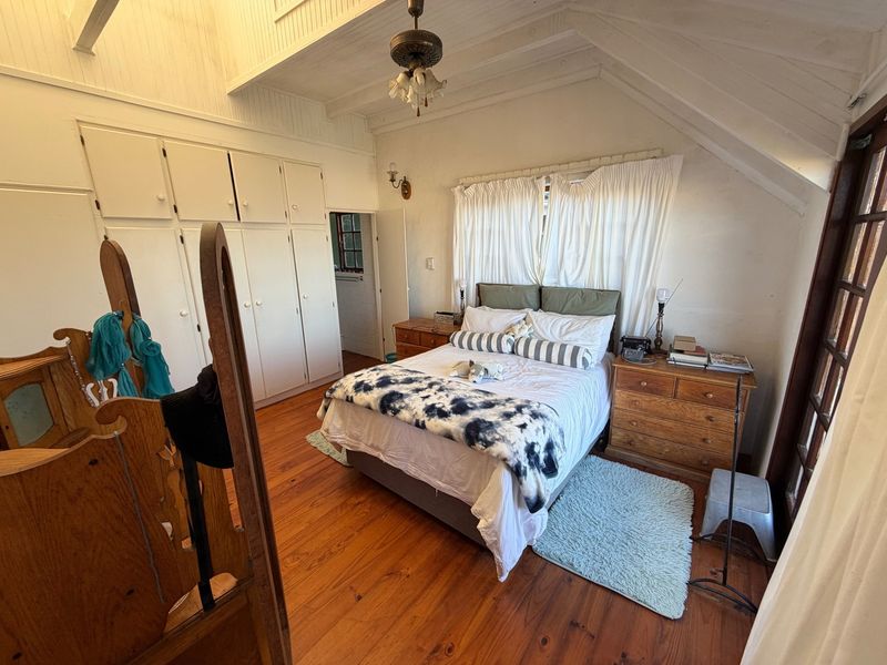 A cozy bedroom featuring timber flooring, vaulted ceilings with exposed rafters, and ample built-in cupboard storage.