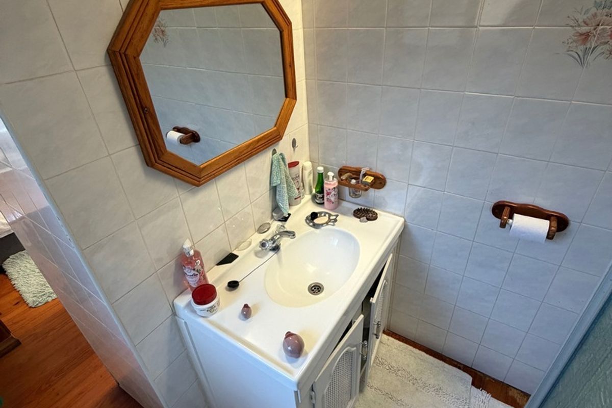 A functional bathroom featuring a vanity cabinet with a ceramic basin, wall-mounted mirror, and tiled walls with timber flooring.