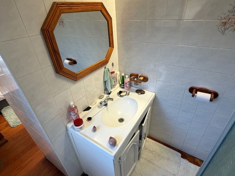 A functional bathroom featuring a vanity cabinet with a ceramic basin, wall-mounted mirror, and tiled walls with timber flooring.