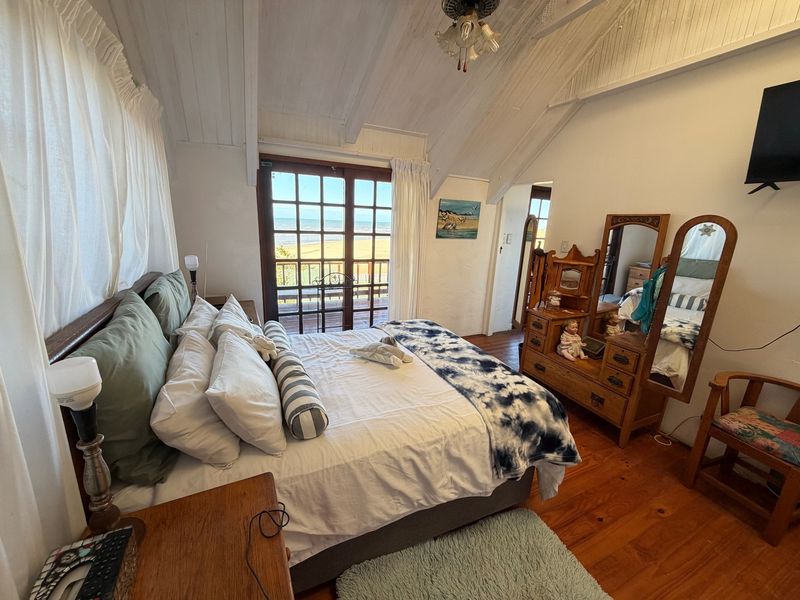 A cozy bedroom featuring vaulted timber ceilings, warm timber flooring, and french doors that open to a scenic coastal view.