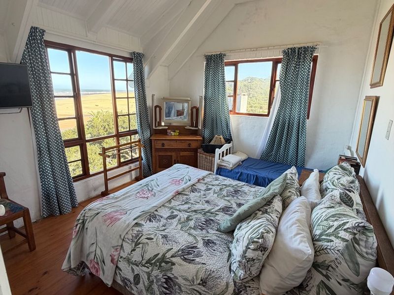 A cozy bedroom featuring timber flooring, a vaulted ceiling with exposed rafters, and large windows offering scenic landscape views.
