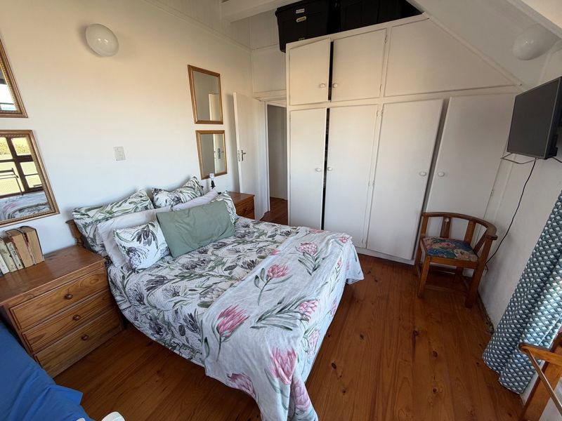 A cozy bedroom featuring warm timber flooring, built-in storage cupboards, and exposed ceiling beams, offering a classic and functional living space.