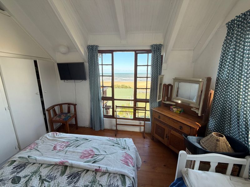 A cozy bedroom featuring timber flooring, a vaulted ceiling, and a large window offering scenic ocean views.