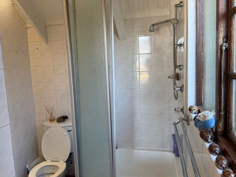 A compact bathroom featuring a shower enclosure, toilet, tiled walls, and timber ceiling details, offering a functional layout with potential for modernization.