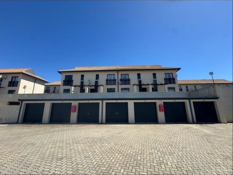 Exterior view of an apartment complex featuring a row of garages with roller doors and upper-level balconies under a clear blue sky.