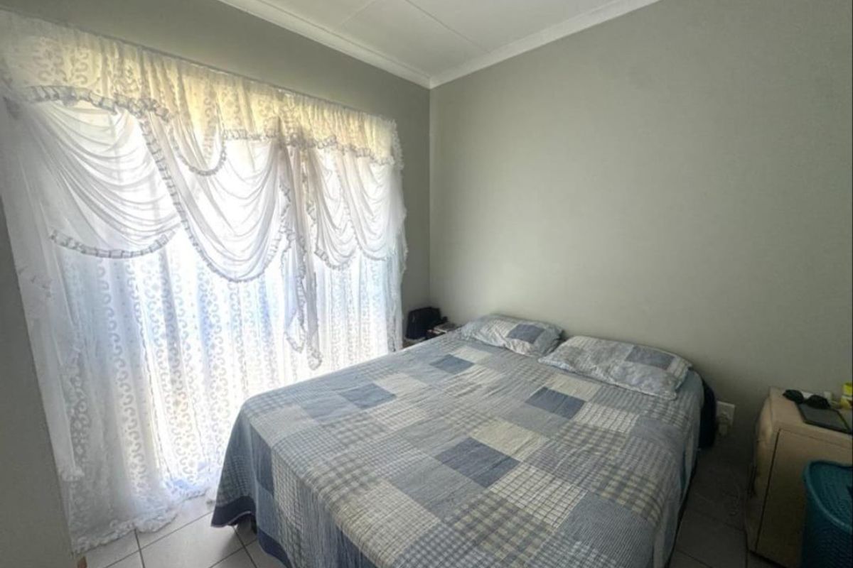 A functional bedroom featuring tiled flooring and a large sliding glass door with decorative curtains, providing natural light to the space.
