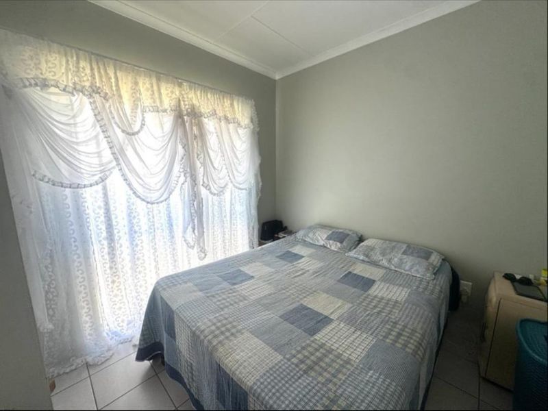 A functional bedroom featuring tiled flooring and a large sliding glass door with decorative curtains, providing natural light to the space.