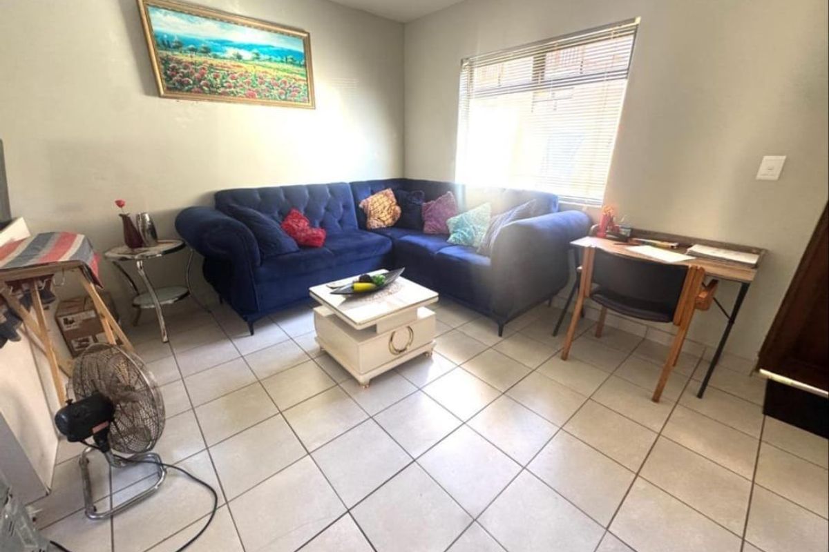 A living room area featuring neutral tiled flooring and a window fitted with venetian blinds, providing a functional and well-lit space.