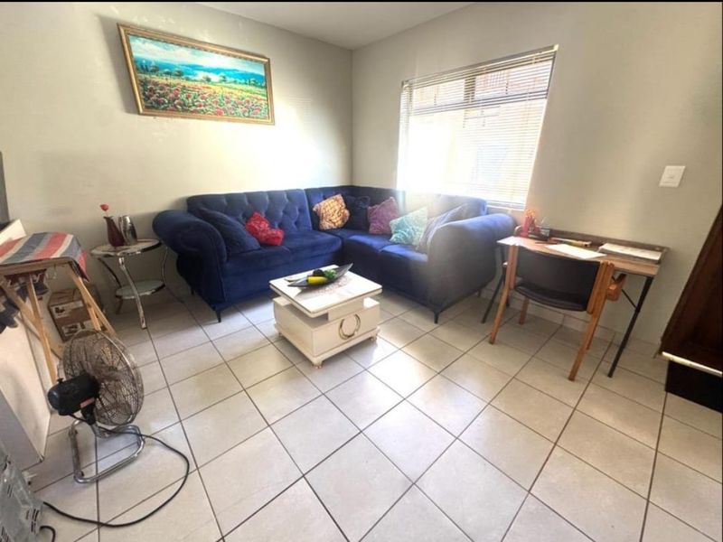 A living room area featuring neutral tiled flooring and a window fitted with venetian blinds, providing a functional and well-lit space.