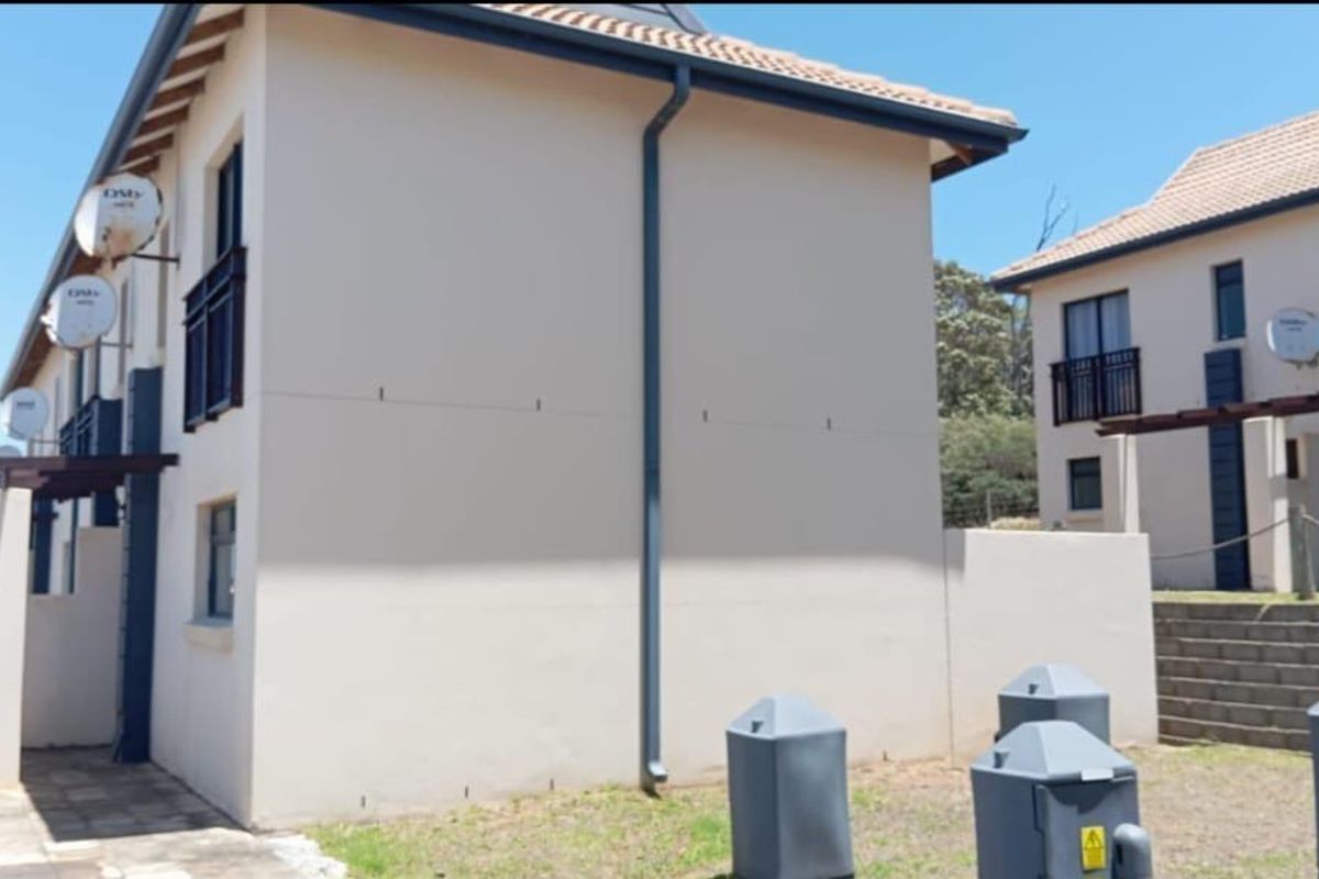 Exterior view of apartment units featuring tiled roofs, satellite dishes, and paved walkways with timber pergola structures.
