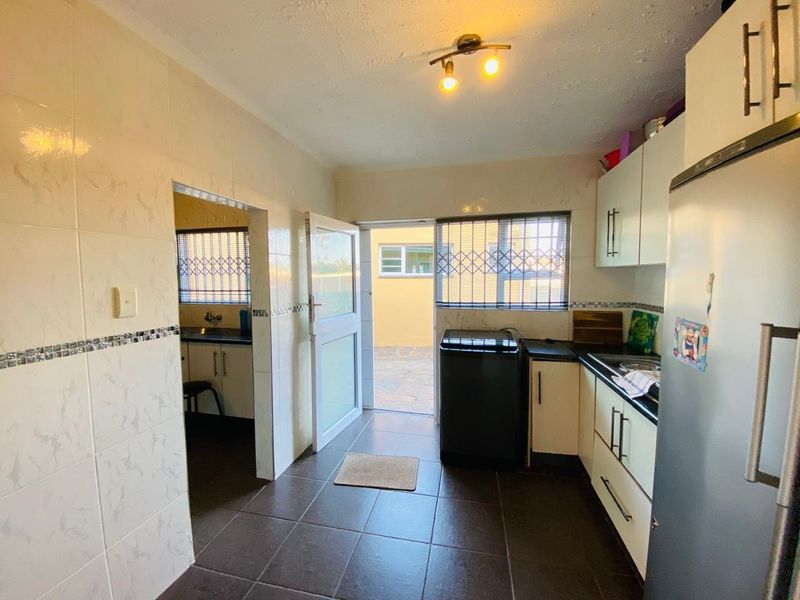 A functional scullery area featuring tiled walls and flooring, built-in cabinetry, and direct access to the exterior through a secure door.