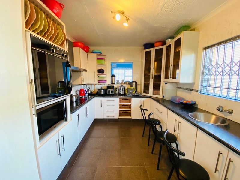 A functional kitchen featuring white cabinetry, built-in oven and microwave, dark countertops, and tiled flooring with a window security gate.