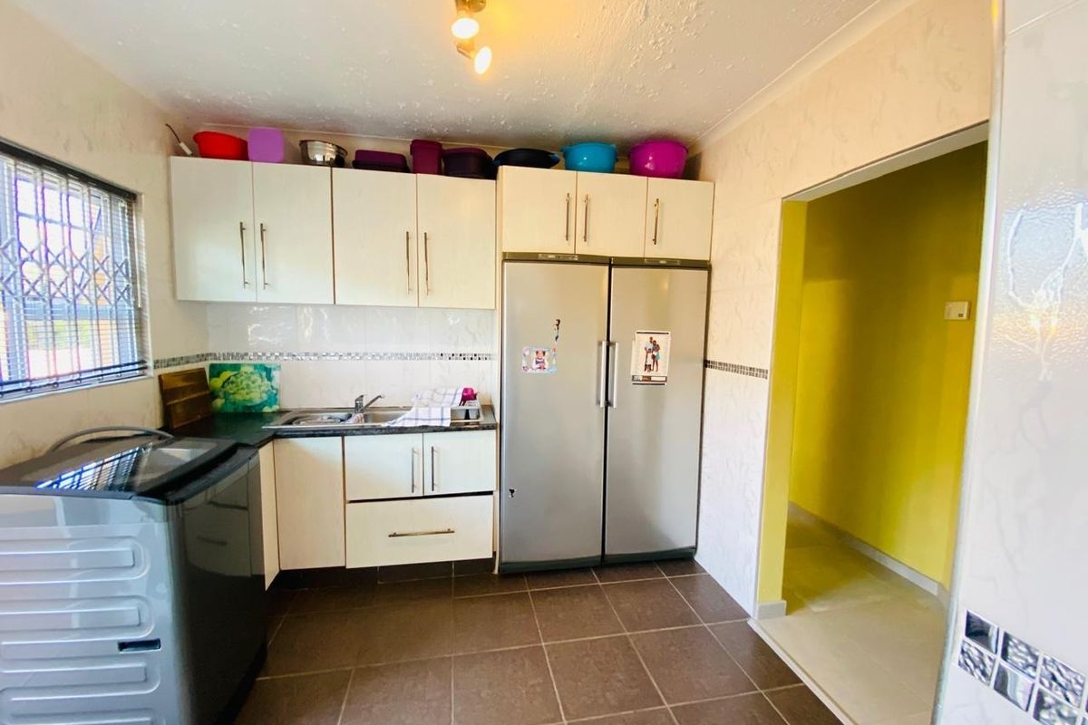A functional kitchen featuring built-in cabinetry, tiled flooring, and a tiled backsplash, with an adjacent doorway leading to another room.