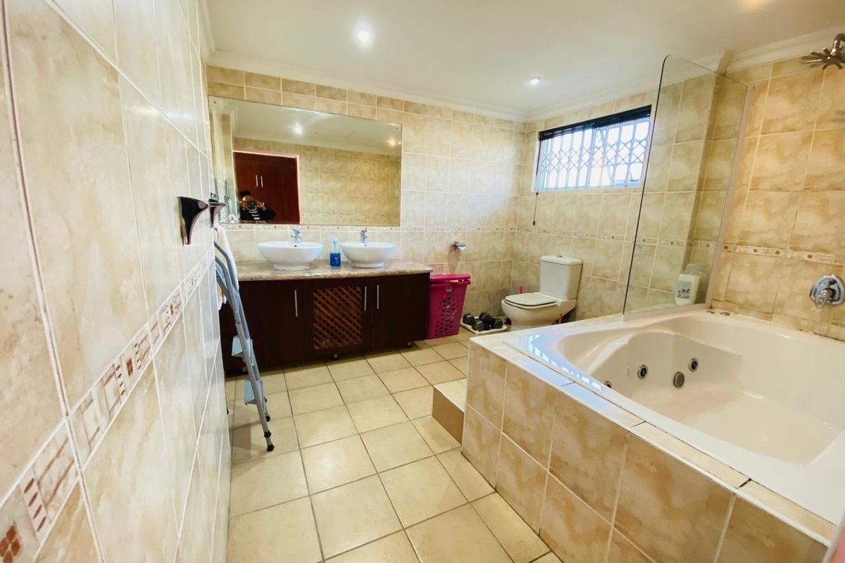 Spacious bathroom featuring a double vanity, large wall mirror, jacuzzi bathtub with glass screen, and neutral floor-to-ceiling tiling.