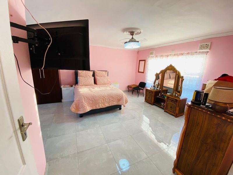 Spacious bedroom featuring light-colored floor tiles, built-in cupboards, and a central ceiling fan, offering a functional layout with ample natural light.