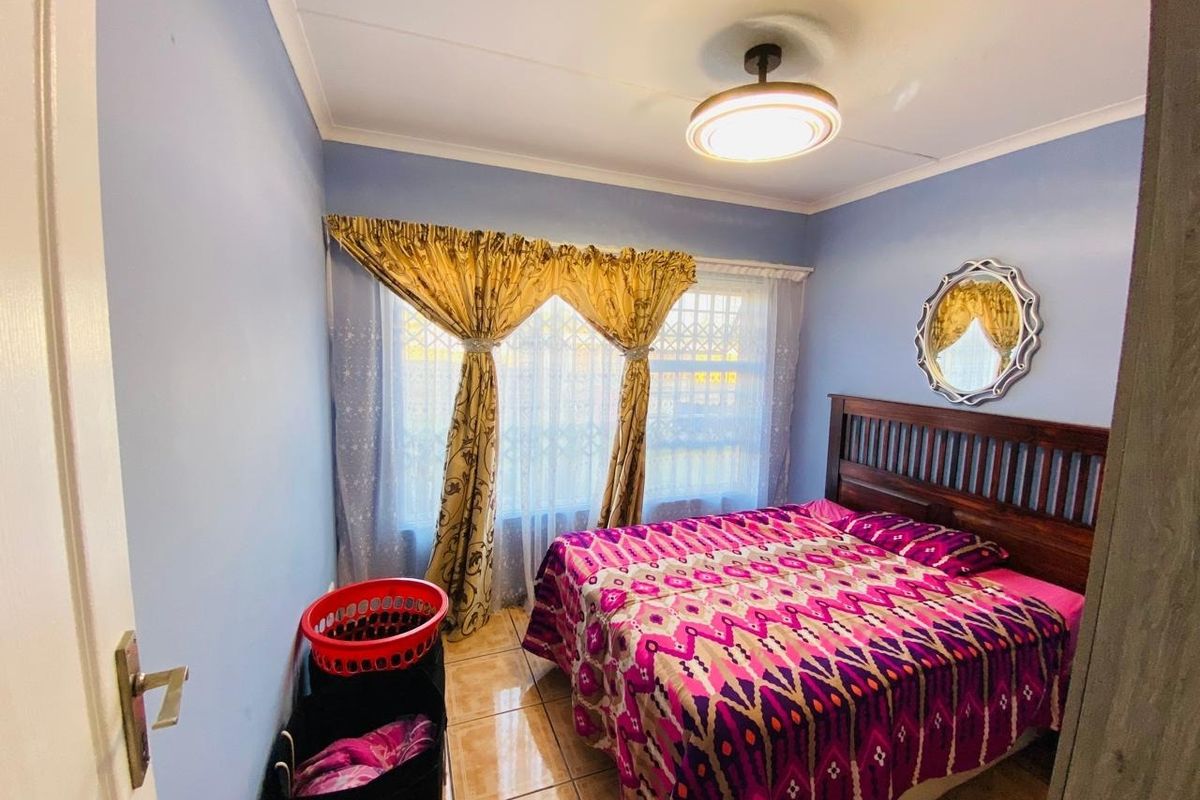 A functional bedroom featuring tiled flooring, a central ceiling light fixture, and a window fitted with a security gate.