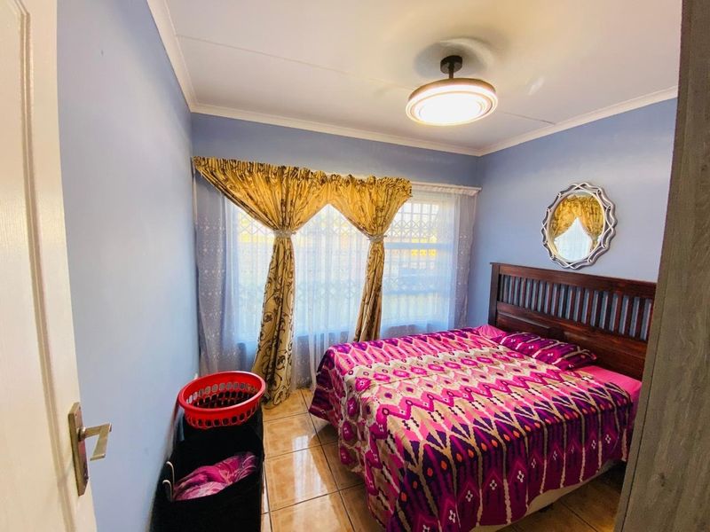 A functional bedroom featuring tiled flooring, a central ceiling light fixture, and a window fitted with a security gate.