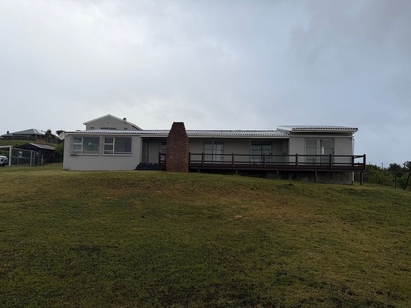 Rear view of the house featuring a large lawn, a prominent brick chimney, and an elevated timber deck with security bars on the windows.