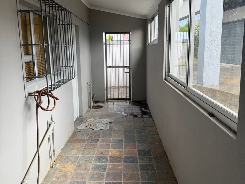 A functional utility corridor featuring tiled flooring, security gates, and large sliding windows, providing a secure and practical transition space.