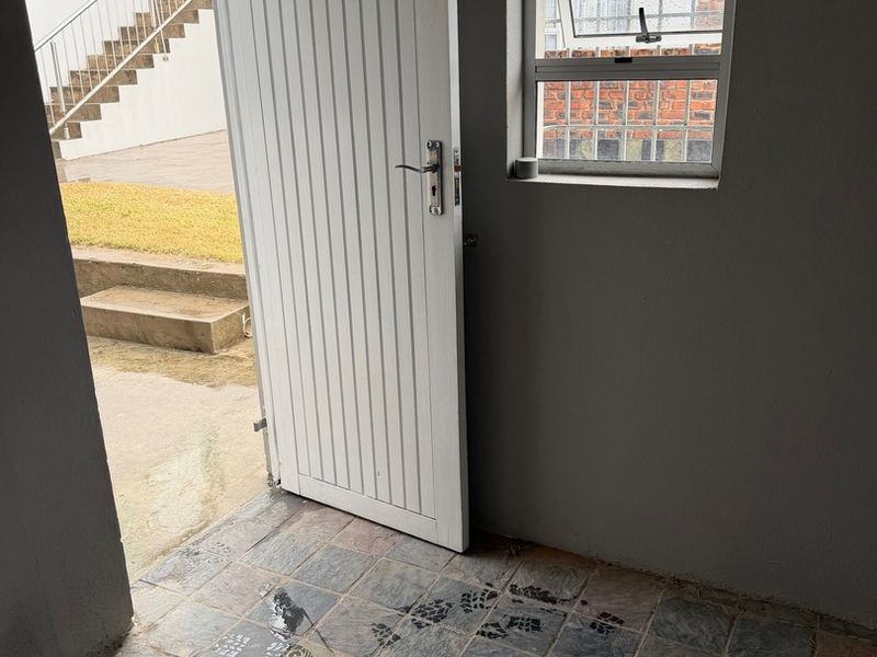 A functional utility space featuring tiled flooring, a secure external door, and a window with burglar bars, providing direct access to the outdoor area.