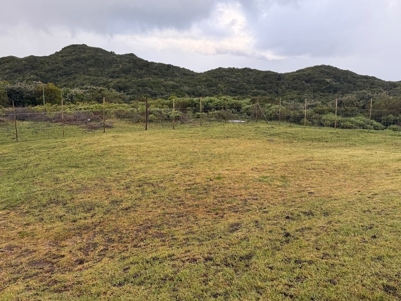 A spacious, open grass garden area enclosed by wire mesh fencing, featuring scenic views of the surrounding hills and natural landscape.