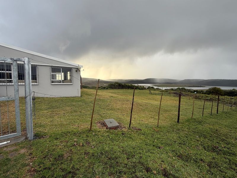 Rear exterior view of the property featuring a large grassy yard, wire fencing, and scenic landscape views under a cloudy sky.
