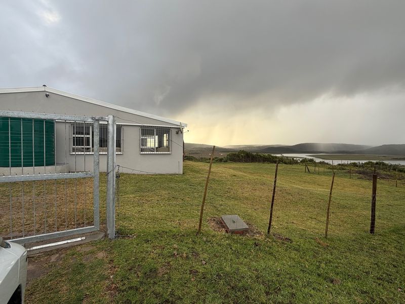 Rear exterior view of the property featuring a water tank, security fencing, and expansive landscape views under a cloudy sky.