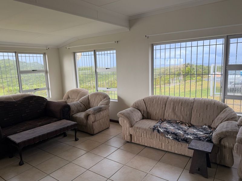 A bright living room featuring tiled flooring and large windows with security bars, offering natural light and views of the surrounding landscape.