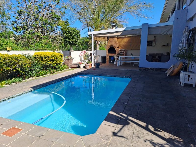 Outdoor entertainment area featuring a swimming pool, paved surround, and a covered patio with a built-in brick braai.