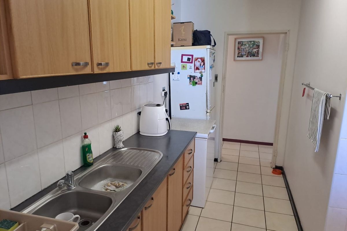 A functional kitchen featuring laminate cabinetry, double bowl stainless steel sink, and tiled flooring, offering a dated aesthetic ready for modernization.