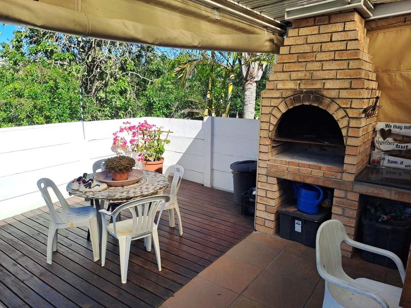 Covered outdoor patio featuring a built-in brick braai, timber decking, and a retractable awning, providing a functional space for outdoor entertaining.