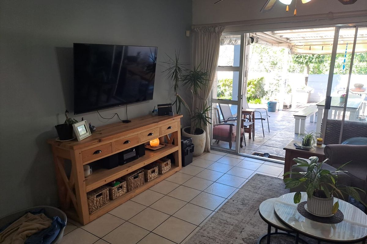 A living room featuring ceramic floor tiles, a ceiling fan, and large sliding glass doors providing direct access to the outdoor patio area.