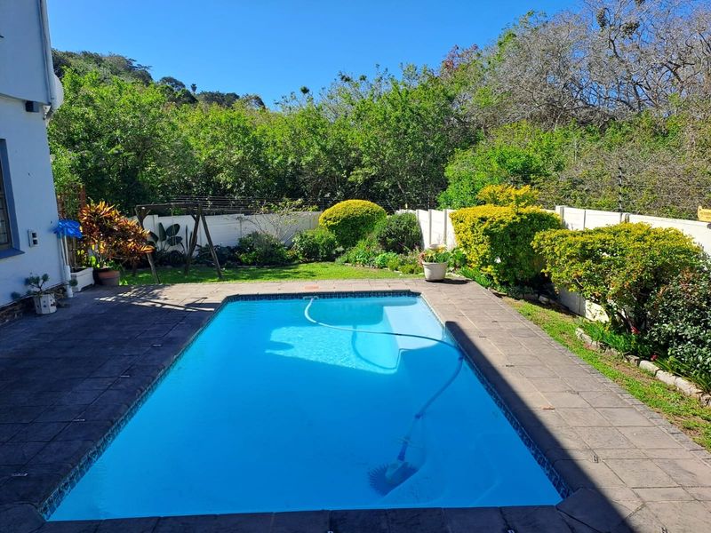 A private outdoor swimming pool area featuring a paved surround, established garden landscaping, and secure perimeter walling with electric fencing.