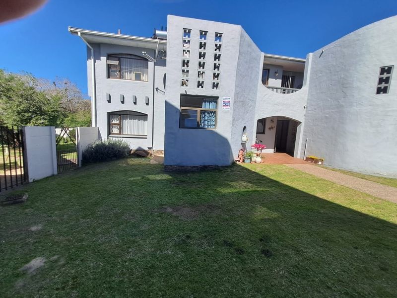 Rear view of the townhouse featuring a lawn, paved walkway, covered patio, balcony, and distinctive breeze block architectural detailing.