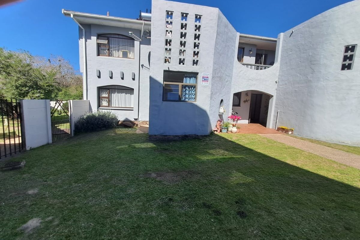 Rear view of the townhouse featuring a lawn, paved walkway, covered patio, balcony, and distinctive breeze block architectural detailing.