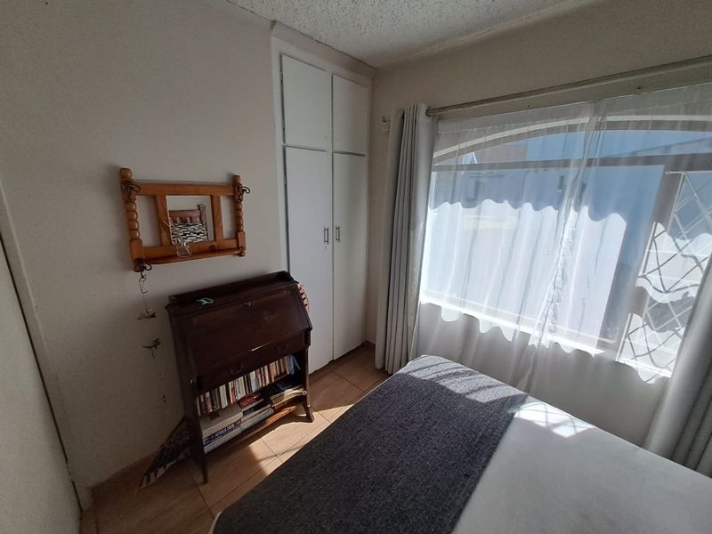 A bedroom featuring built-in cupboards, tiled flooring, and a window with security bars, offering a functional space with potential for modernization.