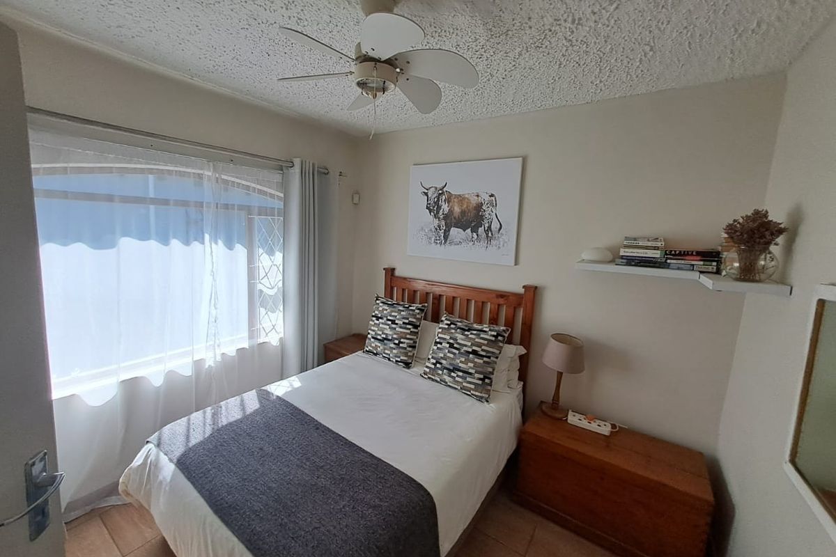 A compact bedroom featuring tiled flooring, a ceiling fan, and a window with security bars, offering a functional and well-lit sleeping space.