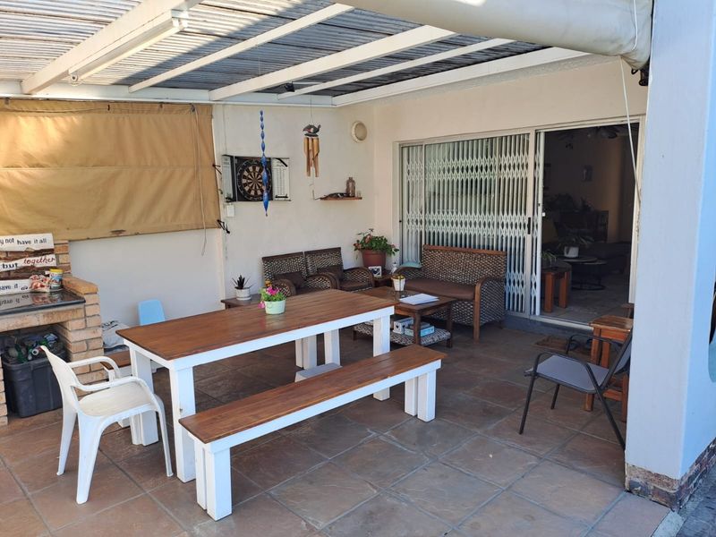 Covered outdoor patio area featuring a built-in brick braai, tiled flooring, and direct access to the interior living space via sliding security doors.