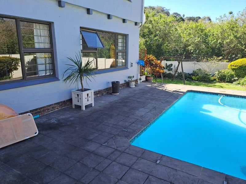 Outdoor pool area featuring a paved patio, swimming pool, and exterior wall with aluminium window frames and security bars.