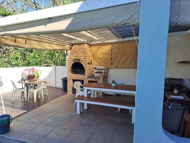 Covered outdoor patio featuring a built-in brick braai, retractable awning, and a combination of tiled and timber deck flooring.