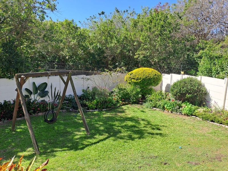 A private rear garden featuring a well-maintained lawn, established garden beds, and secure perimeter boundary walls with electric fencing.