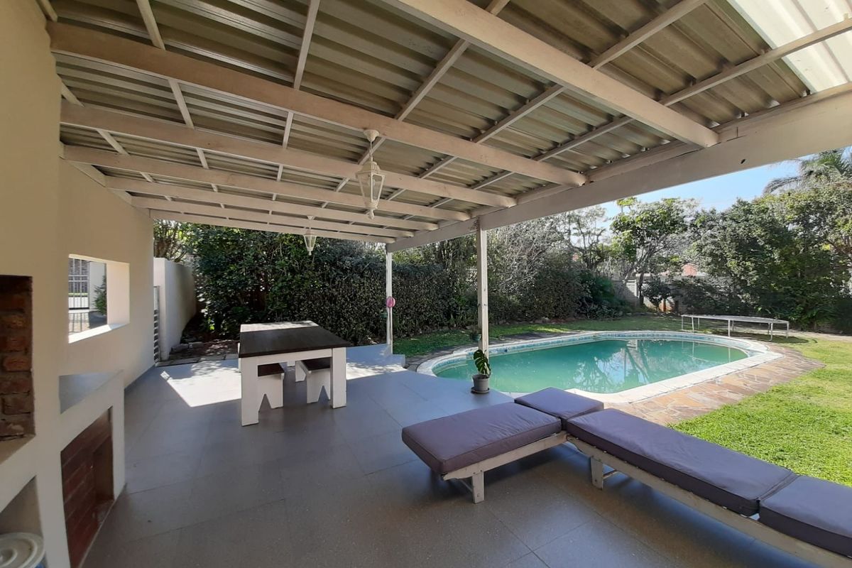 Covered outdoor patio featuring a built-in braai area, overlooking a private swimming pool and garden, ideal for outdoor entertaining.
